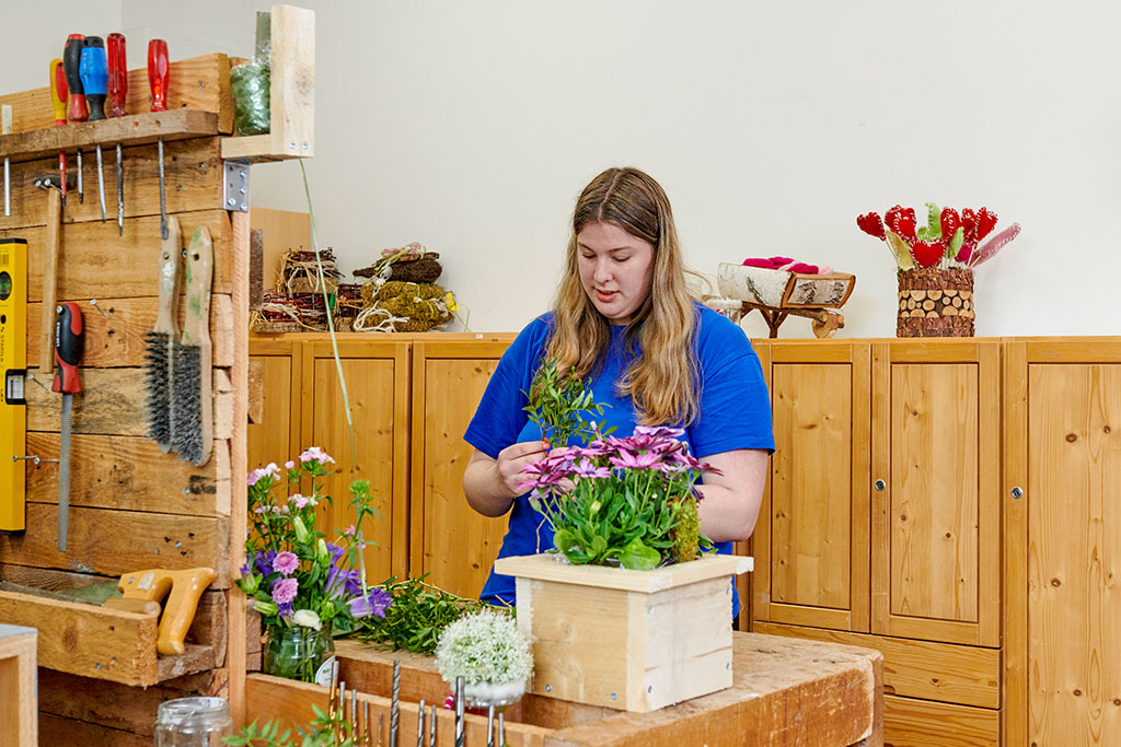 eine junge Frau bepflanzt einen Holzblumenkübel