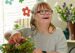 eine lachende junge Frau mit Down-Syndrom arbeitet als Floristin