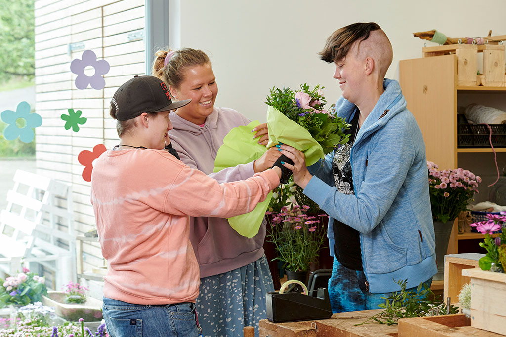 drei Frauen wickeln einen Blumenstrauß in Seidenpapier ein