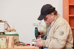 Ein Mann mit Schirmmütze sitzt mit einer Heißklebepistole an einem Werktisch