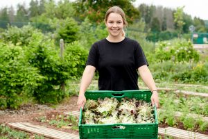 Eine junge Frau trägt eine Kiste mit frischem Salat