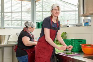 zwei junge Frauen mit roter Schürze wiegen Kräuter klein