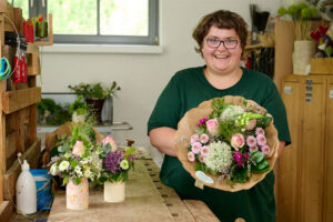 eine fröhliche junge Frau zeigt einen Blumenstrauß
